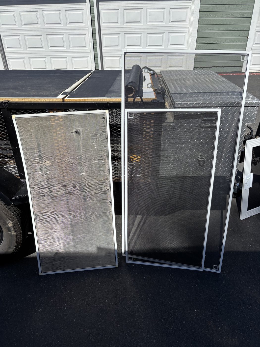 Torn screen next to newly repaired window screens by the screen repair trailer